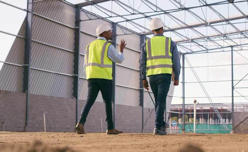 Two people in high visibility vest walking around a construction site.