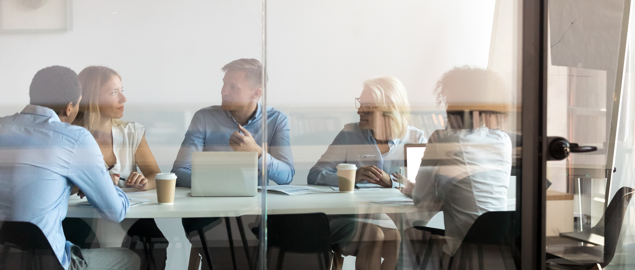 People sitting at a conference room table with coffee and laptops.