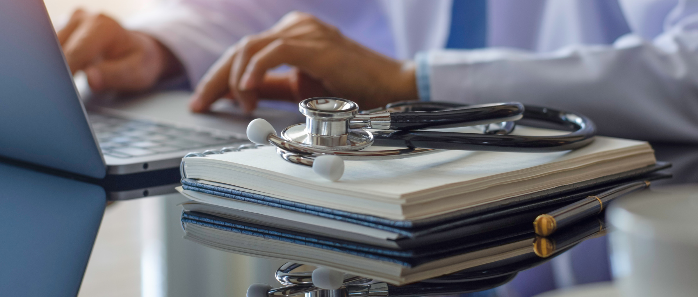 Doctor typing on a computer with a stethoscope laying next to it.