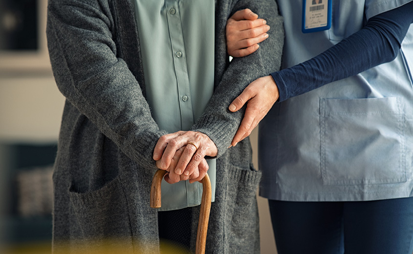 Nurse and person with a cane walking together.