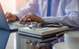 Doctor typing on computer with stethoscope next to it.