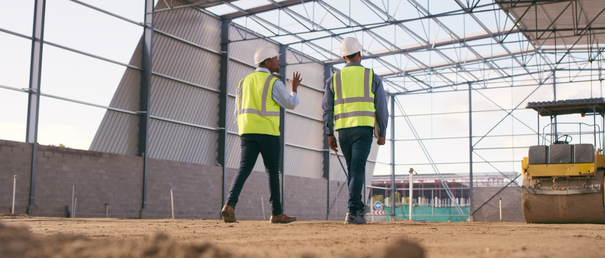 Two people in high visibility vests walking around a construction site.